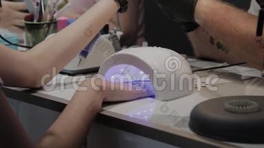 一个年轻的女孩在美甲沙龙的紫外线灯下干指甲油。